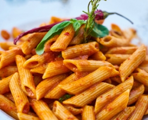 Plato de pasta penne con salsa de tomate y guarnición de albahaca.