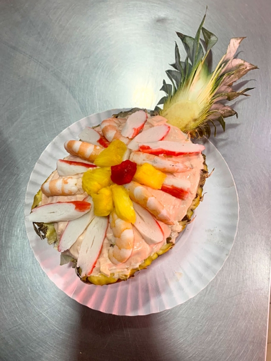 Piña rellena con ensalada de mariscos, incluyendo camarones, surimi y frutas tropicales.