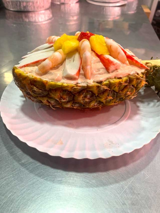 Piña rellena con ensalada de mariscos, incluyendo camarones, surimi y frutas tropicales.